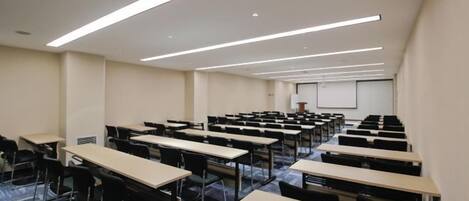 A conference room with rows of tables and chairs, a projector screen, and a whiteboard.