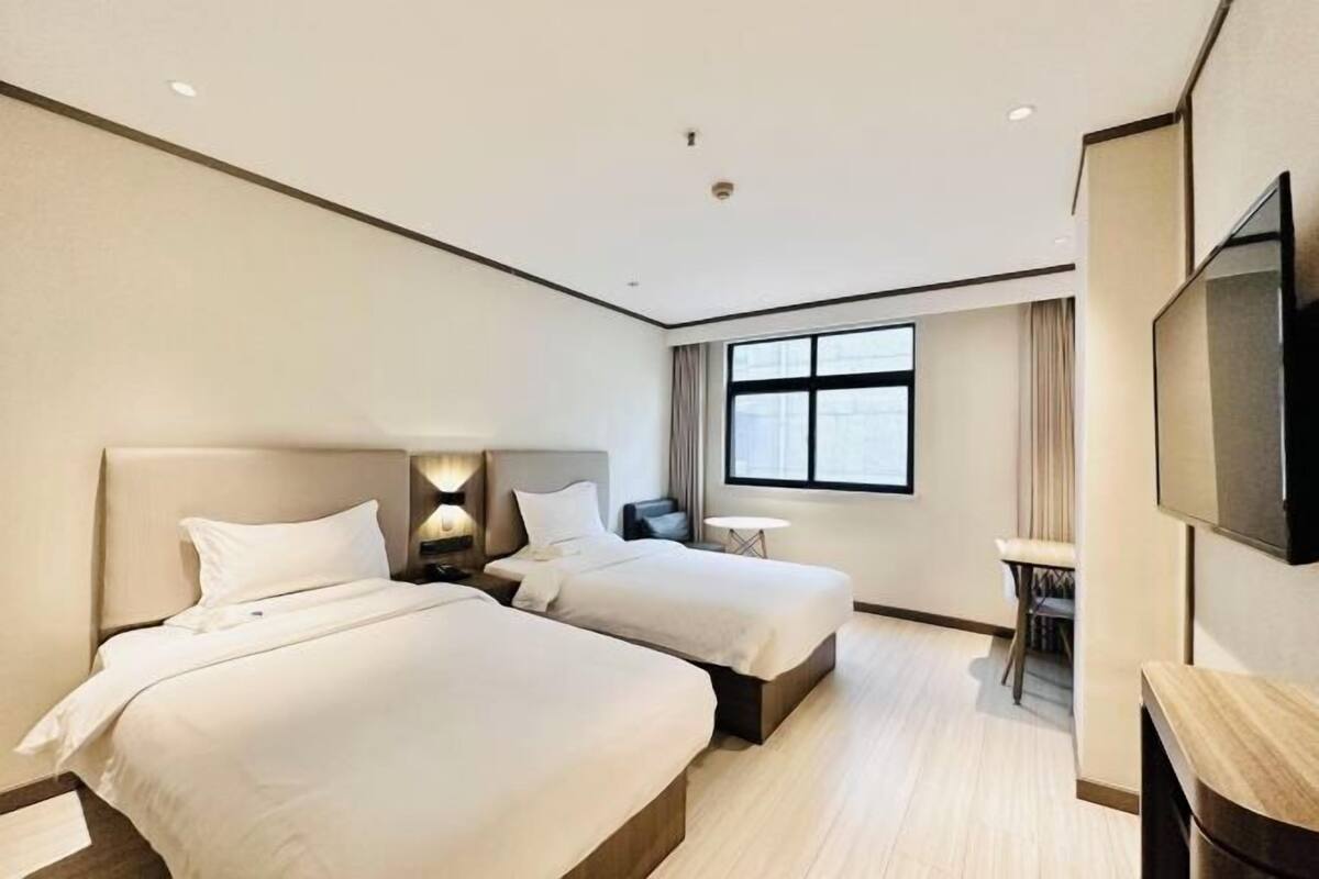 A hotel room with two beds, a desk, a chair, a TV, and a window.