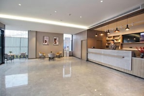 Un hall d’hôtel moderne avec un comptoir d’accueil, un espace salon et une grande fenêtre.