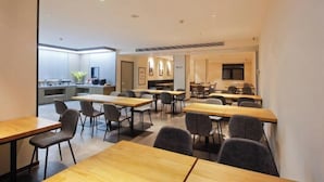 A modern conference room with multiple tables and chairs, a kitchen area in the background, and a large screen on the wall. - HanTing Hotel (Xi'an Bianjiacun Subway Station) (Xi'an)