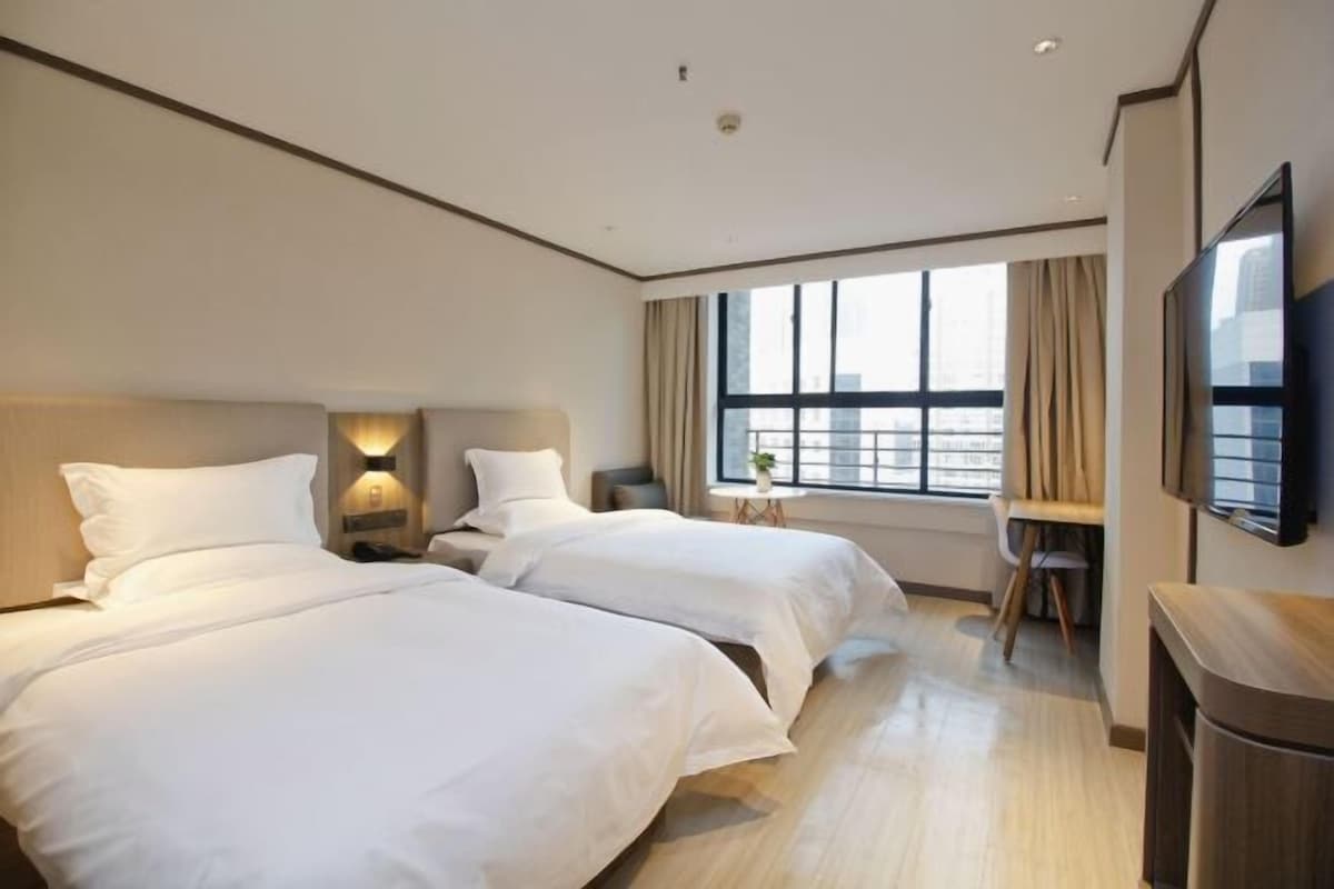 A hotel room with two beds, a desk, a chair, a TV, and a window with curtains.