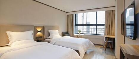 A hotel room with two beds, a desk, a chair, a TV, and a window with curtains.