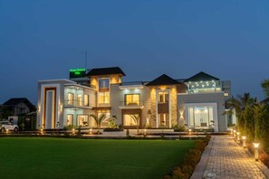 A modern multi-story villa with a well-lit entrance, a driveway, and a landscaped lawn. - Green Galaxy Villa (Amritsar)