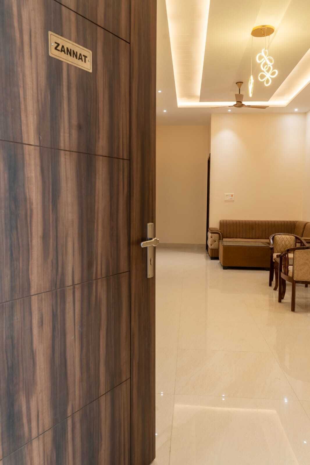 Een modern interieur met een houten deur waarop 'ZANNAT' staat, een bank, stoelen en een plafondlamp.