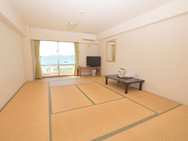A room with tatami mats, a television, a table with items, and a balcony with a view.