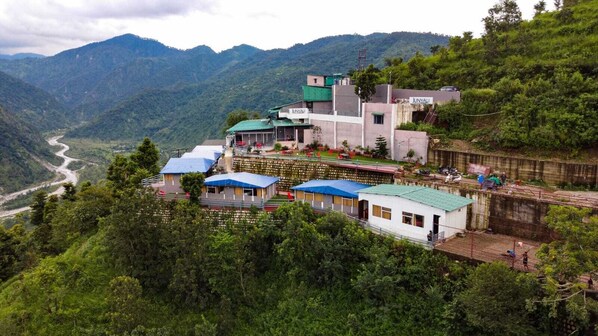 Um hotel com vários edifícios, incluindo uma estrutura principal com telhado verde e vários edifícios menores com telhados azuis. É visível um rio no vale abaixo.