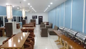 Un grand espace dédié à la salle à manger, avec de longues tables et des bancs en bois, un buffet et un téléviseur fixé au mur.