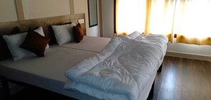 Uma cama com colchão branco e roupa de cama azul, cabeceira de madeira e mesa de cabeceira com abajur.