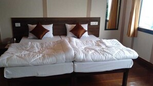 Un lit double avec une literie blanche et deux oreillers marron, une tête de lit en bois et une fenêtre avec des rideaux.