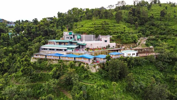 Un hôtel situé sur une colline, composé de plusieurs bâtiments, dont un bâtiment principal doté d’un toit plat et de plusieurs bâtiments plus petits avec des toits bleus.