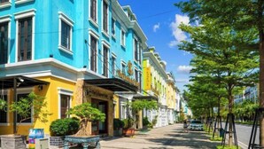 Une rangée de bâtiments aux couleurs vives, bordée d’une rue plantée d’arbres.