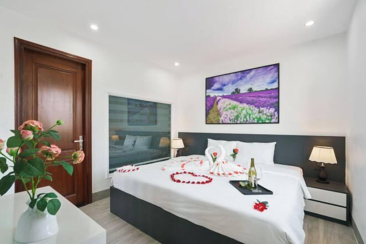 Habitació d'hotel amb un llit, un quadre, un vas amb flors i una taula de nit.