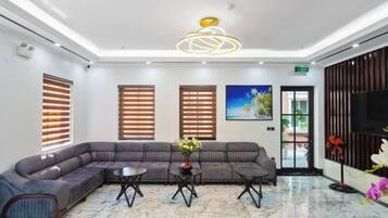 Un vestíbulo de hotel con un sofá modular, dos mesas auxiliares, un cuadro grande y un televisor en la pared.