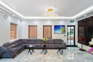 A hotel lobby with a sectional sofa, two coffee tables, a large painting, and a television on the wall. - The Enchanted Ha Long Hotel - Bai Chay Beach (Bai Chay)