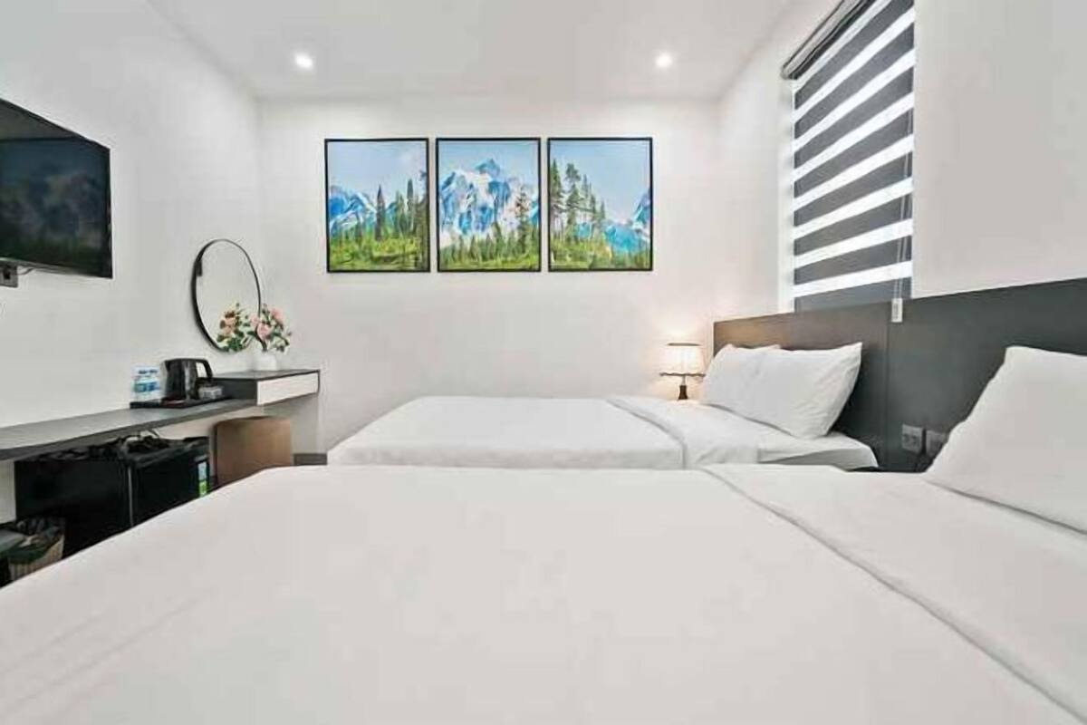 Una habitació d'hotel amb un llit, una taula de treball amb un ordinador i una televisió. Hi ha tres quadres amb marc a la paret.