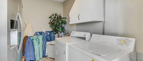 A laundry room with a washer and dryer, a drying rack, and a plant.