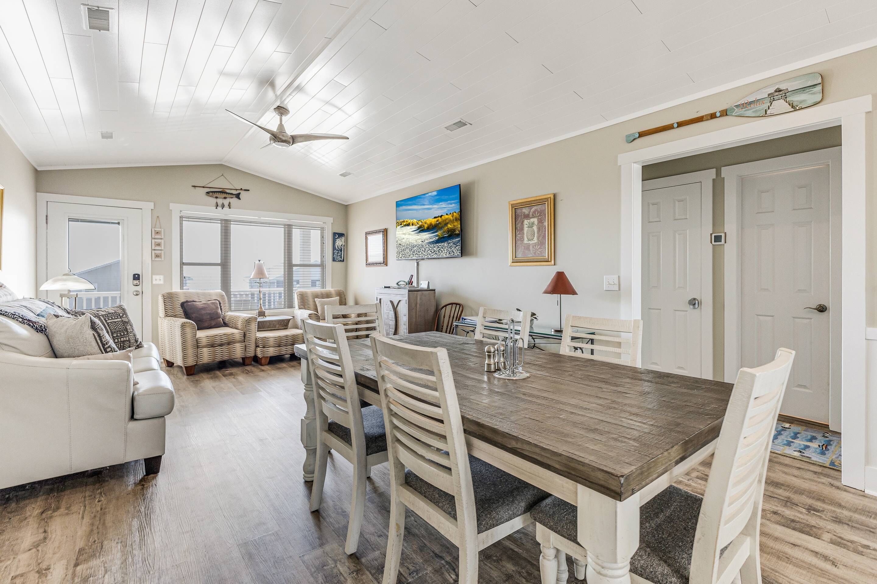 A spacious dining area with a wooden table and white chairs, a ceiling fan, and a large window with a view.