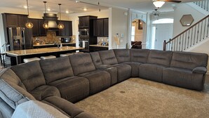 A spacious living room with a large sectional sofa, a kitchen with dark cabinets, and a staircase leading to another level. - Spacious 5-bedroom, 8-bed house in welcoming Grovetown, w/ Rogue fitness room (Grovetown)