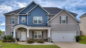 A two-story house with a front porch, a garage, and a stone foundation. - Spacious 5-bedroom, 8-bed house in welcoming Grovetown, w/ Rogue fitness room (Grovetown)
