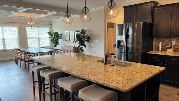 A modern kitchen with a granite island, dark cabinetry, stainless steel appliances, and pendant lighting. - Spacious 5-bedroom, 8-bed house in welcoming Grovetown, w/ Rogue fitness room (Grovetown)