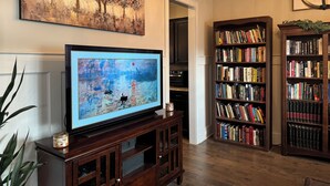 A living room with a television, bookshelves, and a painting. - Spacious 5-bedroom, 8-bed house in welcoming Grovetown, w/ Rogue fitness room (Grovetown)