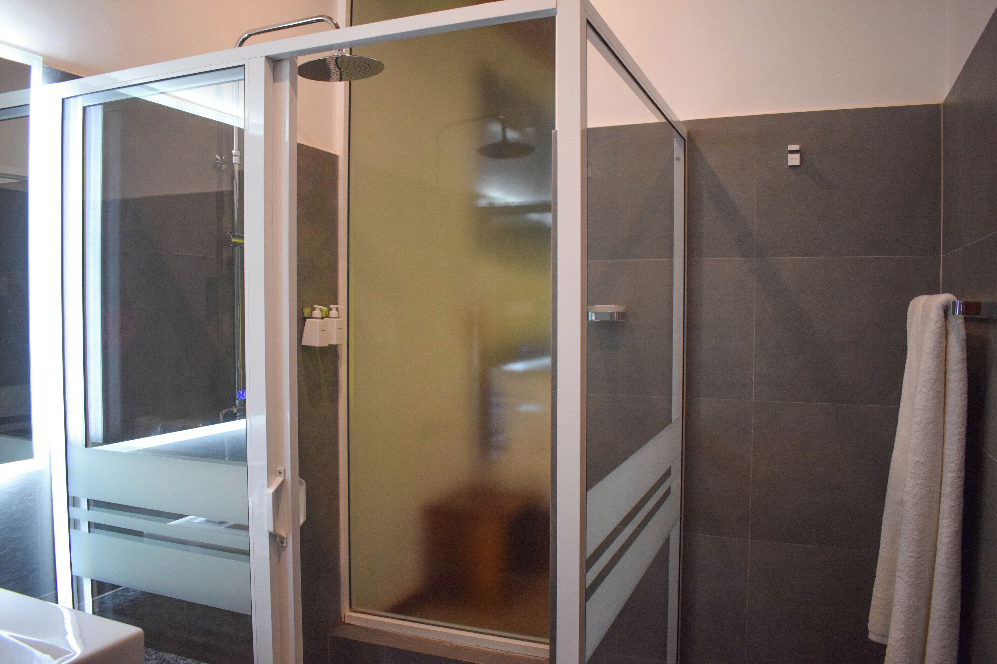 A modern bathroom with a glass shower enclosure, a white sink, and a towel hanging on the wall.