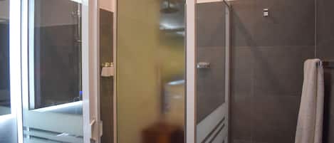 A modern bathroom with a glass shower enclosure, a white sink, and a towel hanging on the wall.