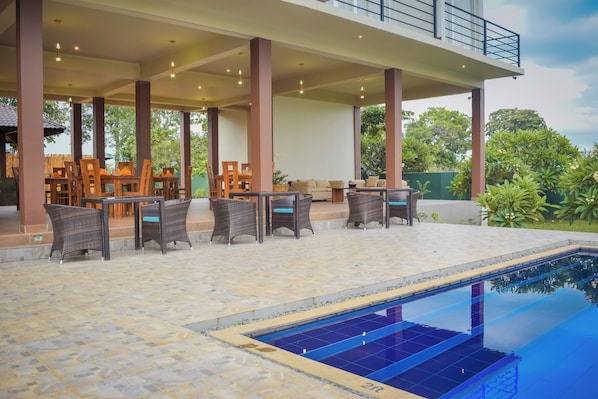 Un área junto a la piscina con suelo de baldosas, sillones de descanso y una piscina.