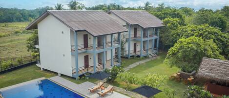 A hotel with a swimming pool, multiple balconies, and a thatched-roof structure.