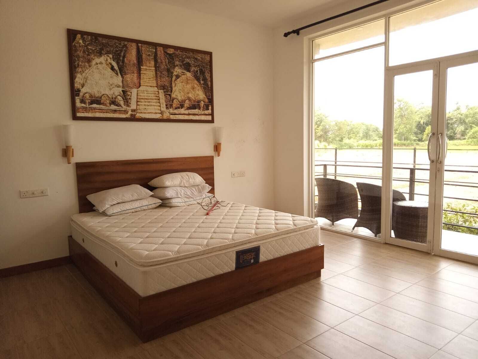 Une chambre avec un lit en bois, une grande fenêtre et un tableau accroché au mur.