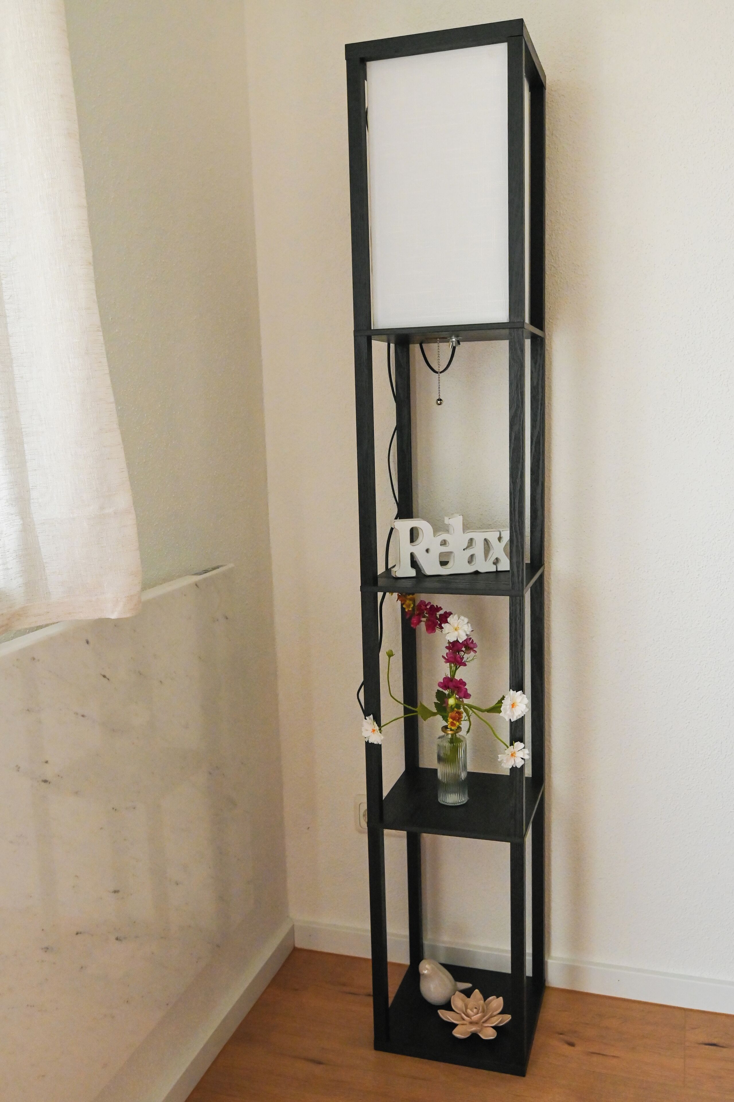 A black metal shelf unit with a 'Relax' sign, a vase with flowers, and decorative items on the lower shelf.