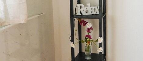 A black metal shelf unit with a 'Relax' sign, a vase with flowers, and decorative items on the lower shelf.