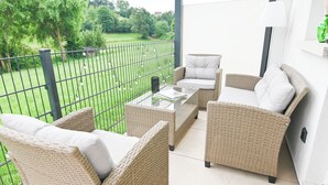 Ein Balkon mit Korbmöbeln, einem Glastisch und Blick auf einen grünen Garten.