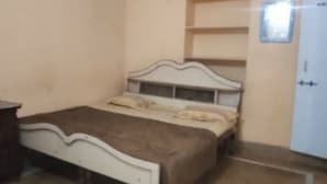 Een eenpersoonsbed met hoofdeinde en voetenbalk, een nachtkastje en een kledingkast tegen een effen muur.