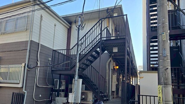 Un edificio de varios pisos con una escalera metálica que lleva a un nivel superior. Hay bicicletas estacionadas afuera y una escalera en el suelo.