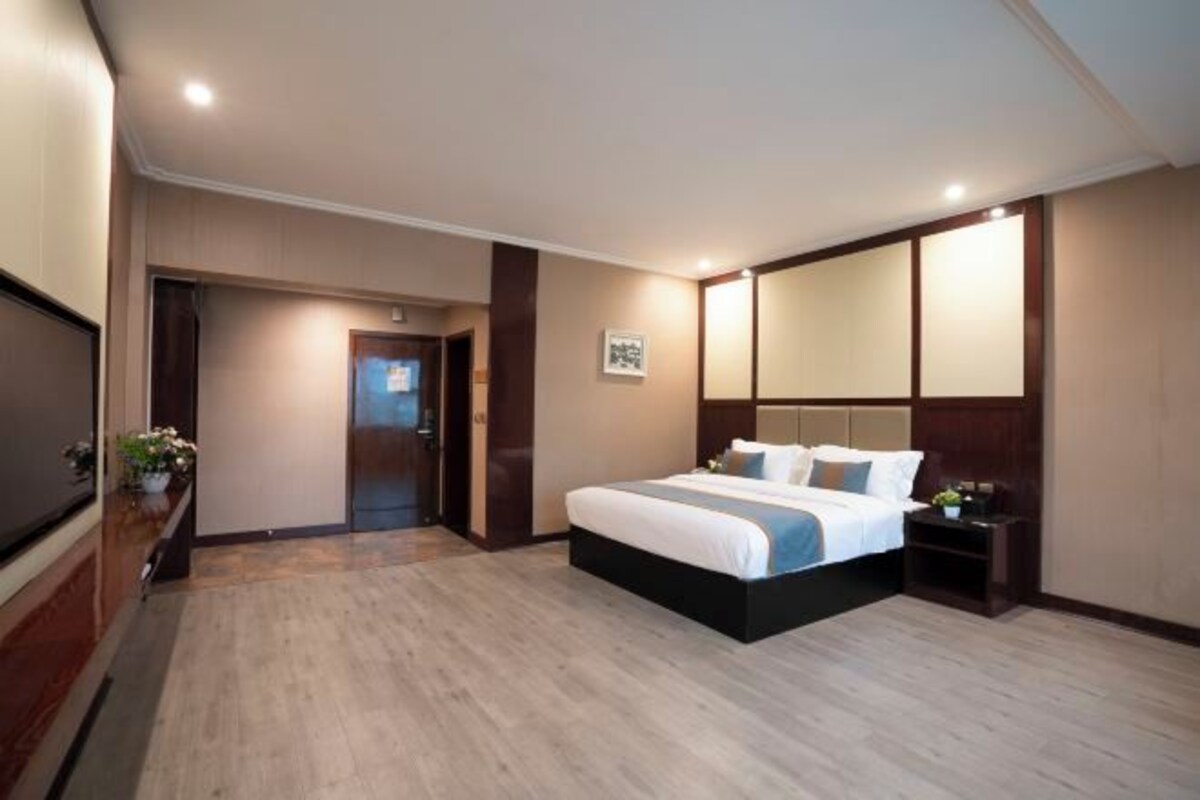A hotel room with a large bed, a TV, a desk, and a mirror.