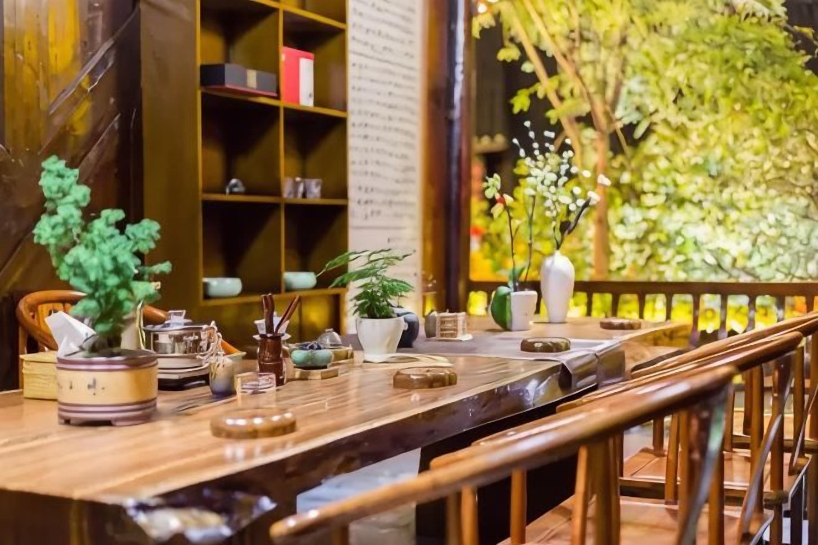 Une table en bois sur laquelle se trouvent divers objets, une bibliothèque et une vue sur la verdure.