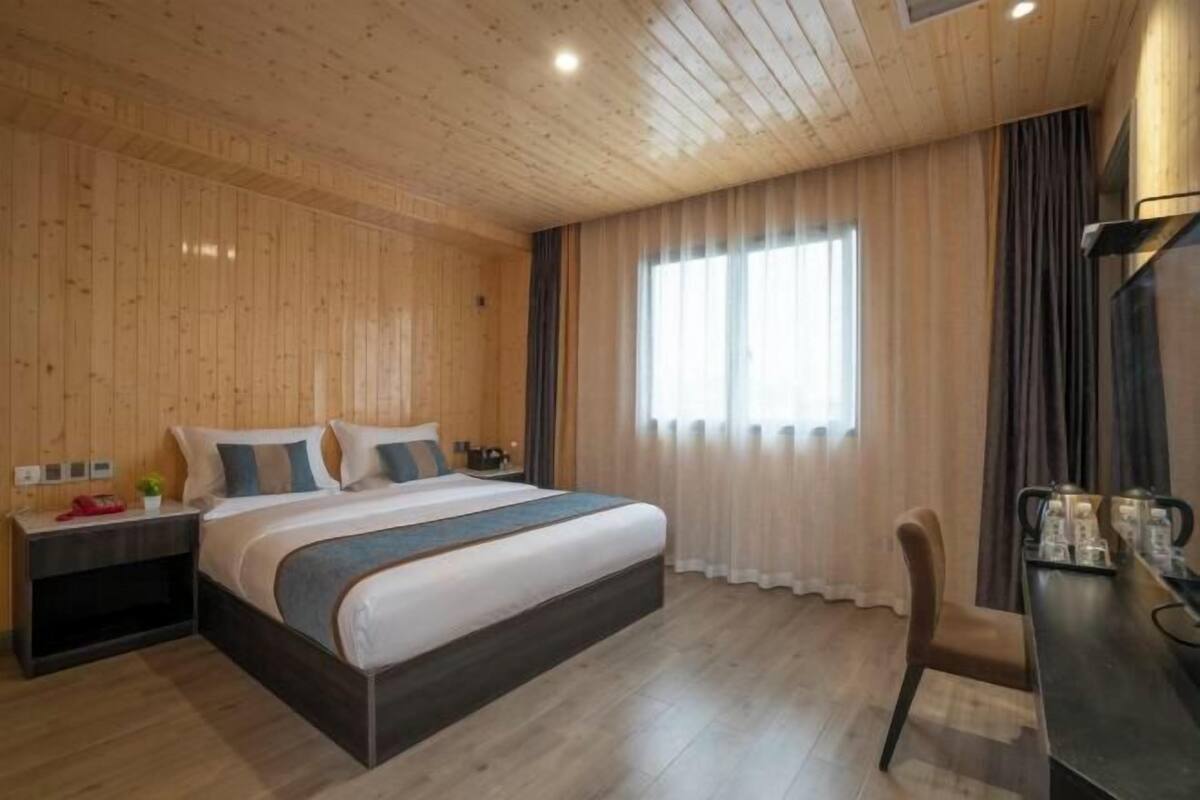 A wooden-paneled room with a bed, bedside table, and a window with curtains.