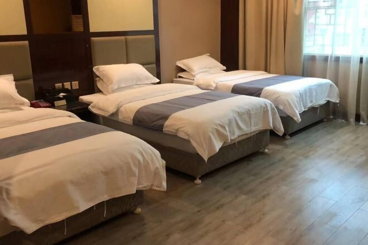 A hotel room with three single beds, a wooden floor, and a large window with curtains.