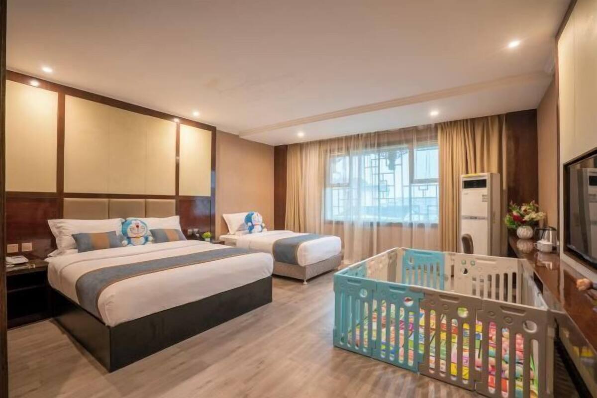A hotel room with two beds, a crib, a television, and a window with curtains.