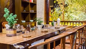 A wooden table with tea sets and a potted plant, a bookshelf in the background, and a wooden railing. - Siji Xiaozhu Hotel (Danzhai)