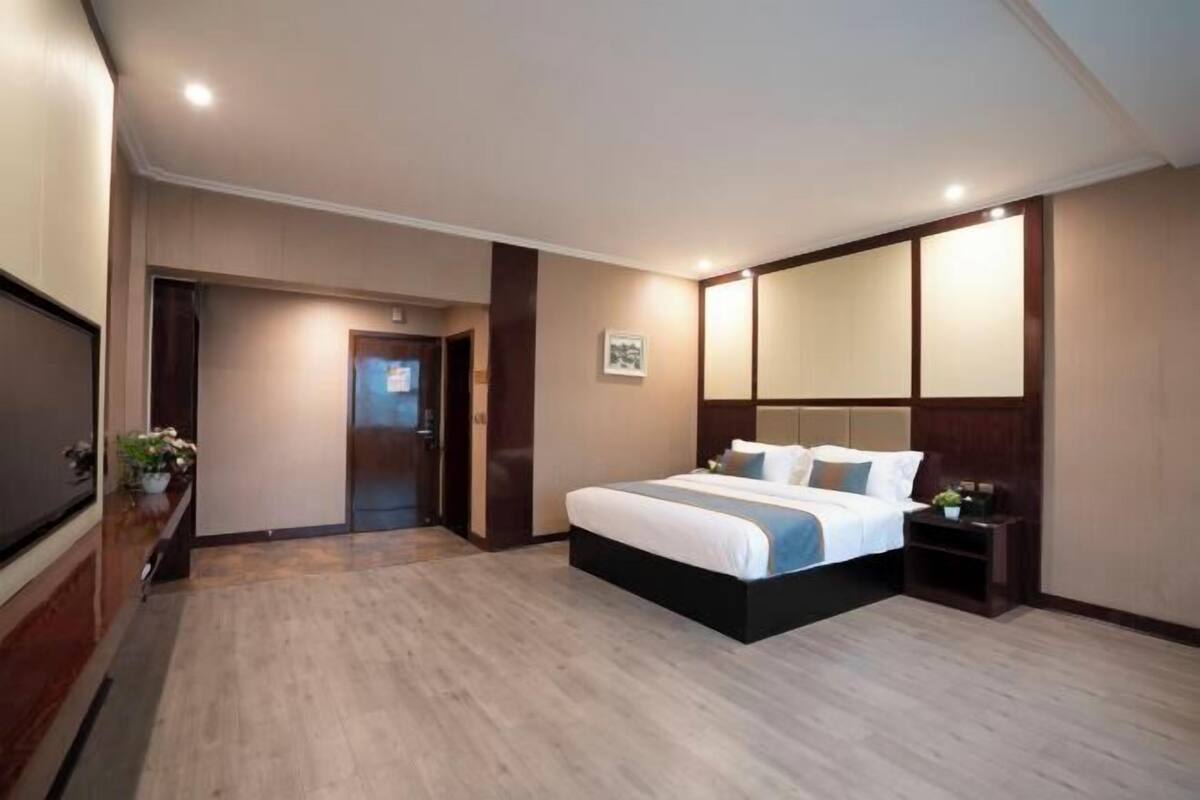 A hotel room with a large bed, a TV, a wooden floor, and a mirror above the bed.