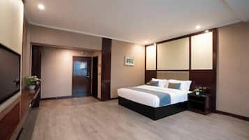 A hotel room with a large bed, a TV, a wooden floor, and a mirror above the bed.
