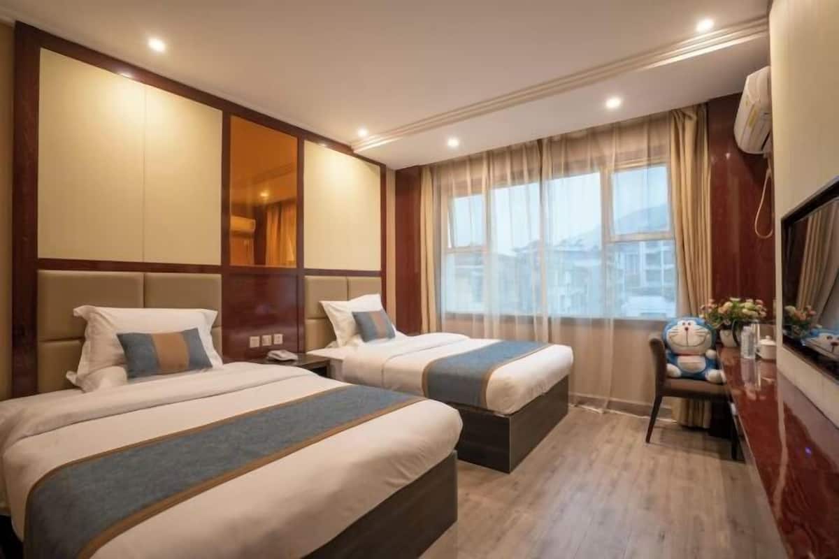 A hotel room with two beds, a desk, and a large window.