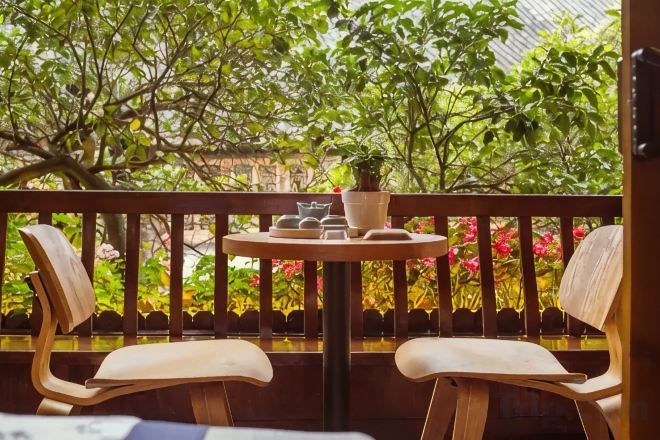 A balcony with two wooden chairs, a small round table with a potted plant, and a view of lush greenery.
