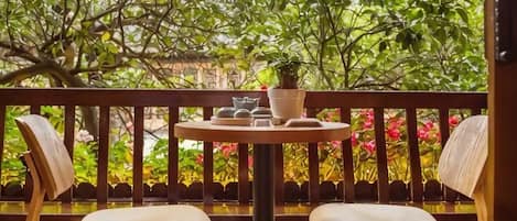 A balcony with two wooden chairs, a small round table with a potted plant, and a view of lush greenery.