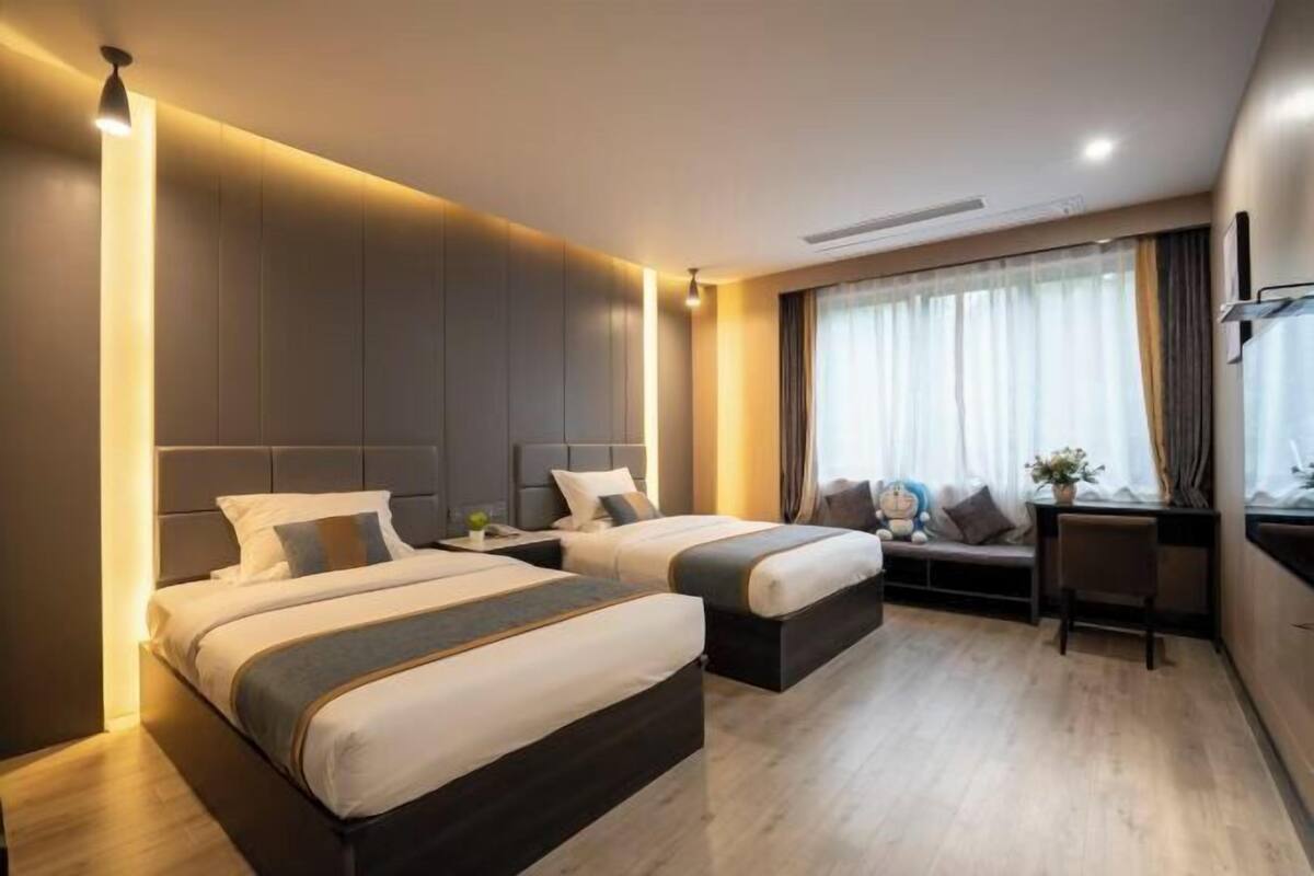 A modern hotel room with two beds, a desk, and a large window with curtains.