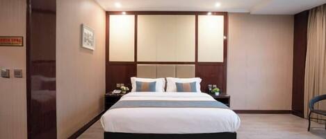A hotel room with a large bed, a headboard with built-in lighting, a nightstand with a lamp, and a chair.