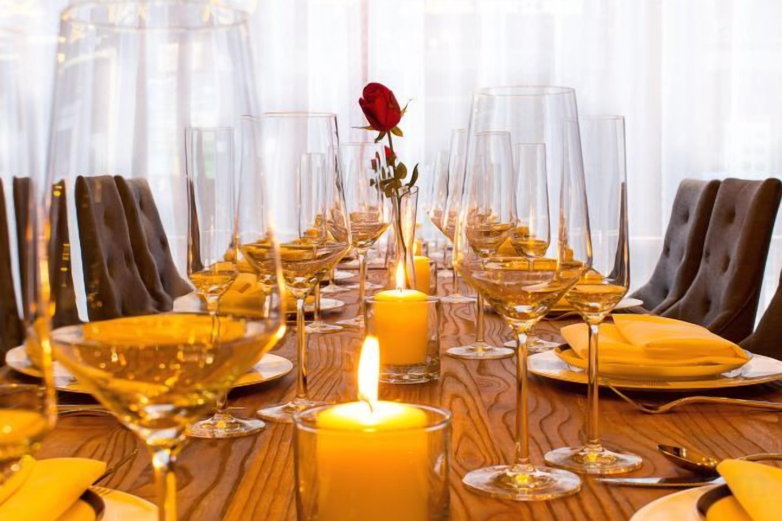 A dining table set with wine glasses, a candle, and a rose.