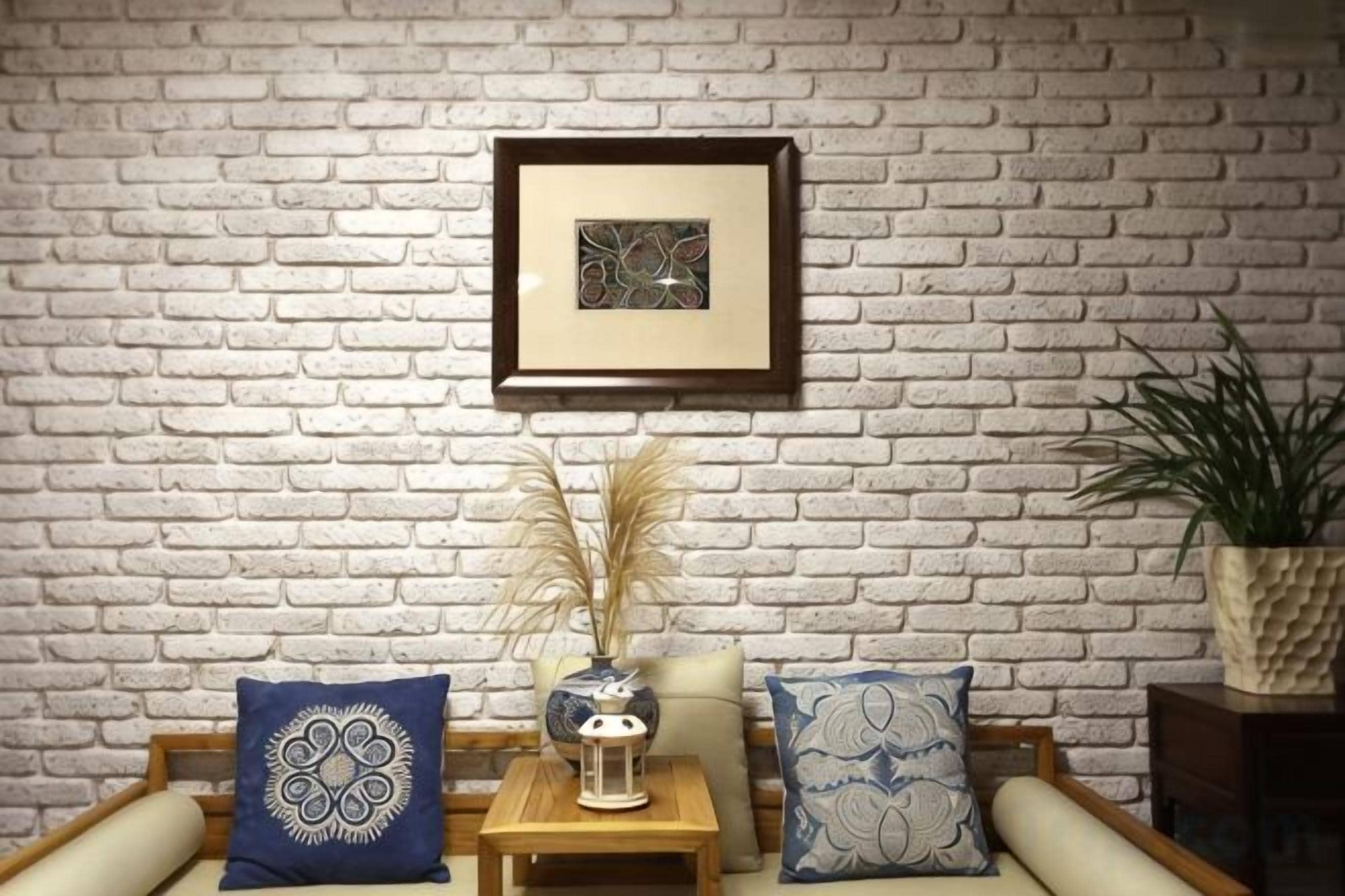 A room with a white brick wall, a framed picture, a small table with a vase, and a potted plant.